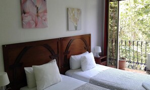 A hotel room with two beds, a wooden headboard, white bedding, and a balcony with a view of greenery. - Hostal Absolut Stay - Adults Only (Barcelona)