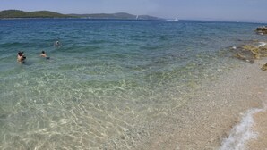 A beach with clear shallow water, a sandy shore, and a distant view of a sailboat. - Villa Vicina (Milna)