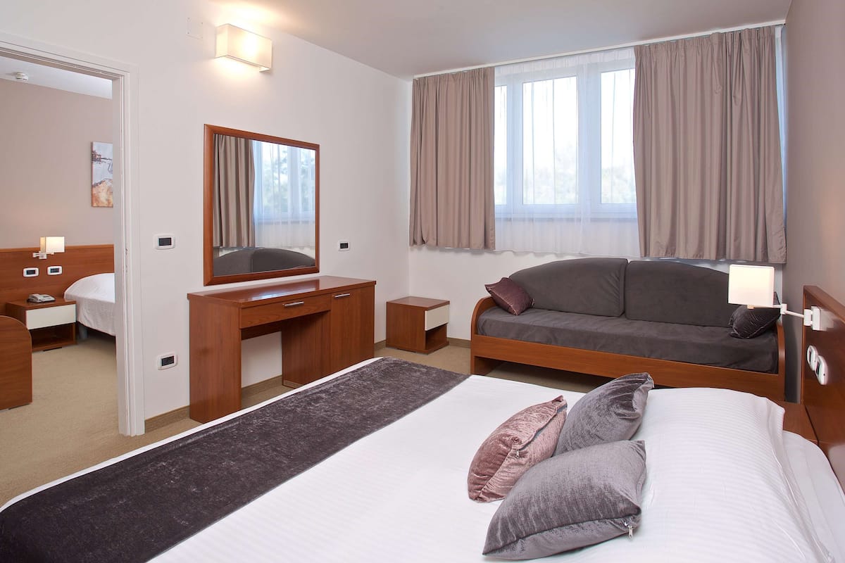 Une chambre d’hôtel avec un lit, un bureau, un canapé et une grande fenêtre avec des rideaux.