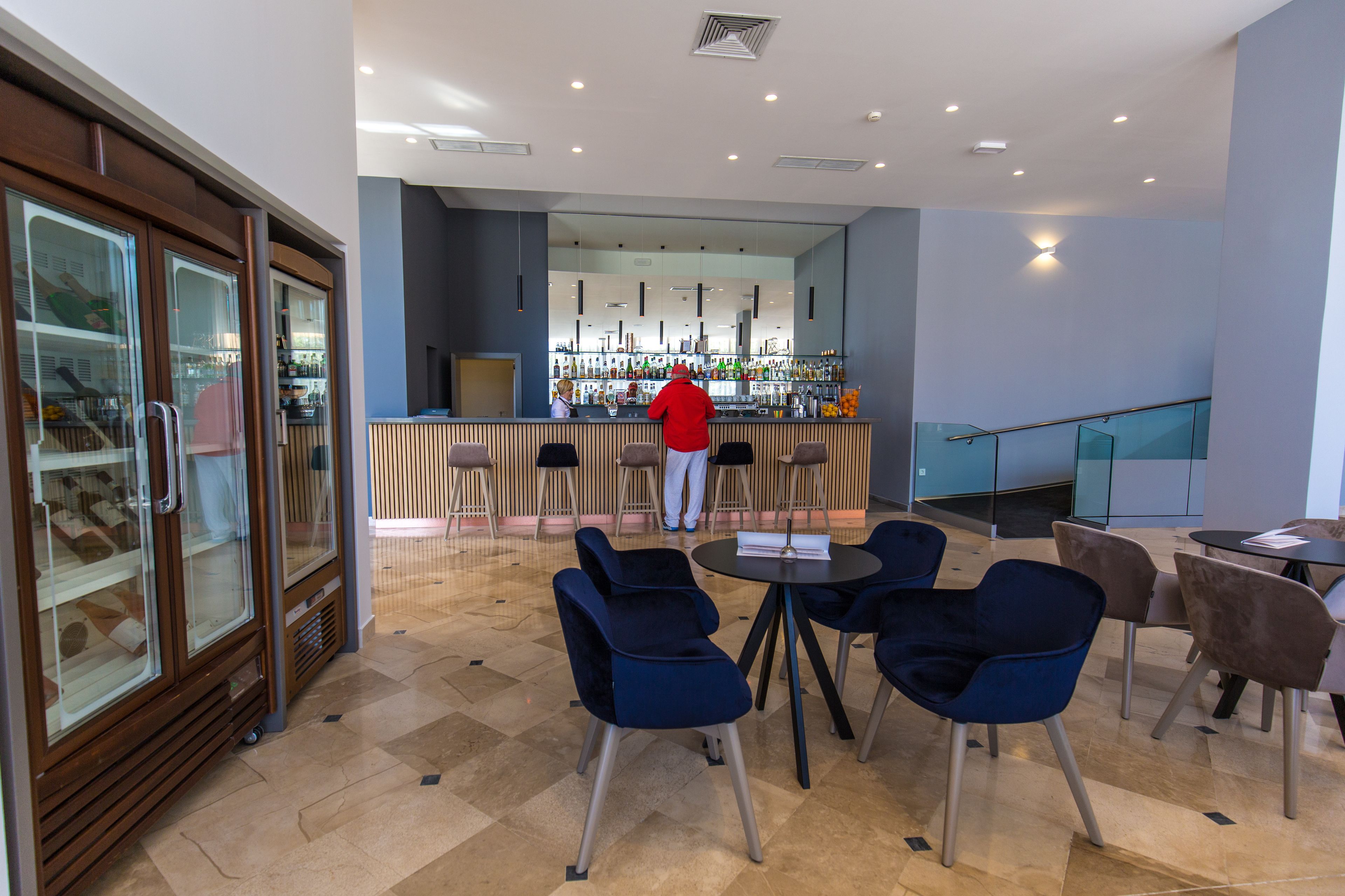 A modern bar area with a bartender, blue and brown chairs, and a glass display case.