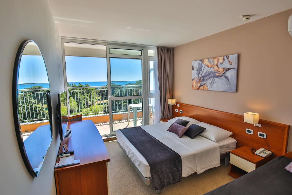Une chambre d’hôtel avec un grand lit, un bureau, une chaise et un balcon donnant sur la mer.