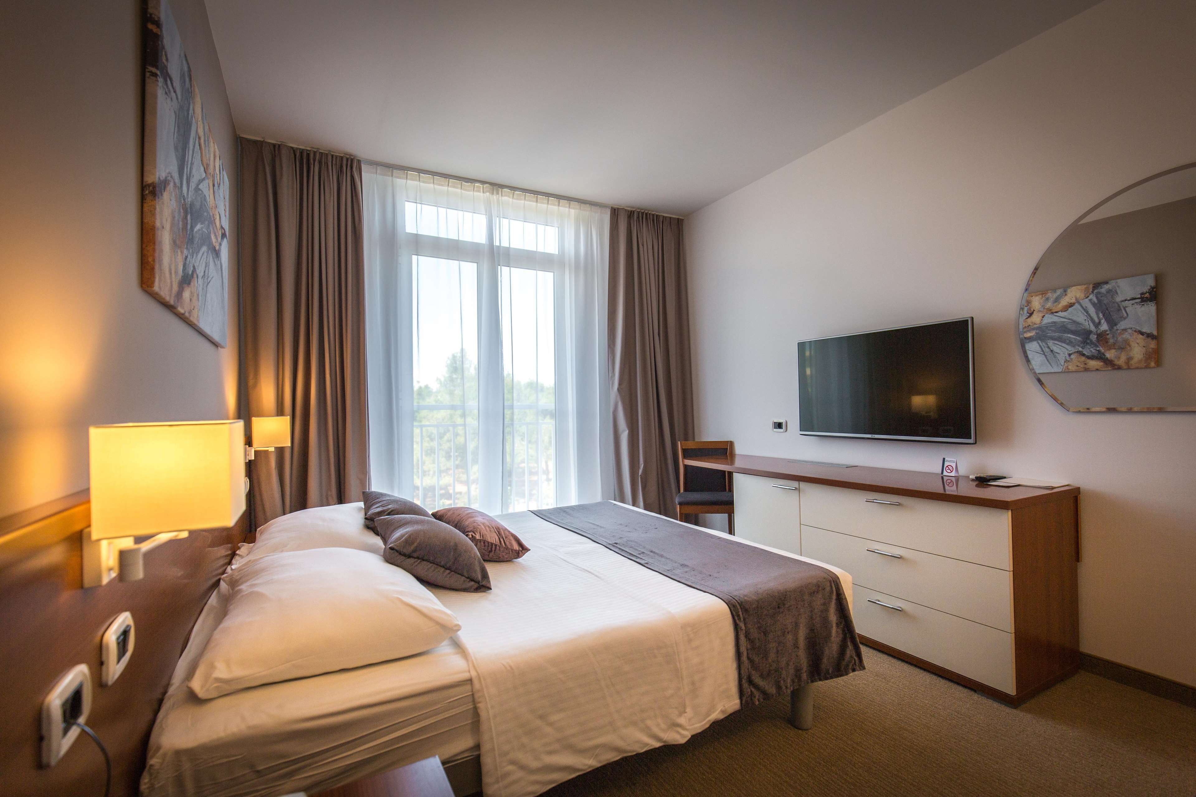 Ein Hotelzimmer mit einem Bett, einem Schreibtisch, einem Fernseher und einem Fenster mit Vorhängen.