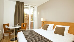 Une chambre d’hôtel avec un lit, un bureau avec un ordinateur portable, une chaise et une fenêtre avec des rideaux.