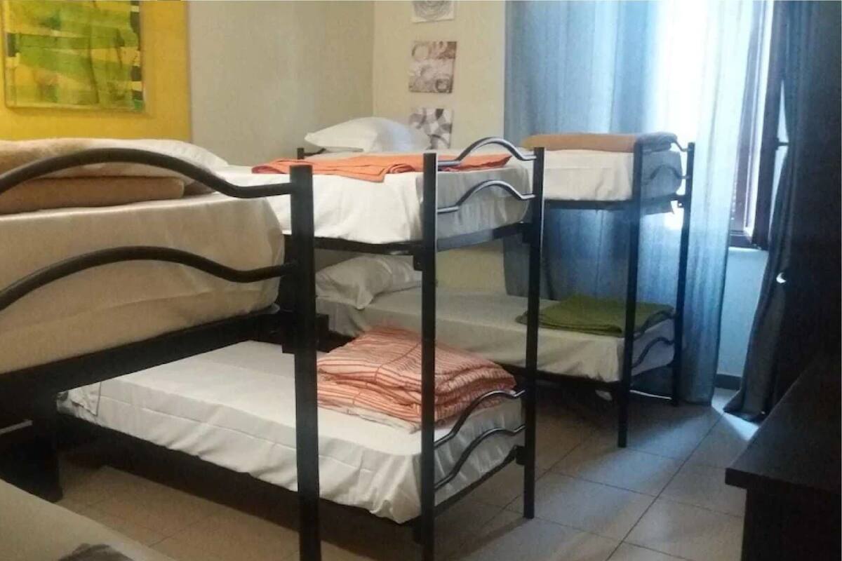 A dormitory room with bunk beds, a bed, a chair, and a window with curtains.