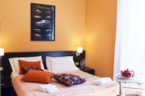 A hotel room with a bed, pillows, a nightstand, a lamp, and a poster on the wall. - San Lorenzo Guest House (Rome)