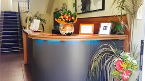 A reception desk with a vase of flowers, a framed certificate, and a plant to the right. - San Lorenzo Guest House (Rome)