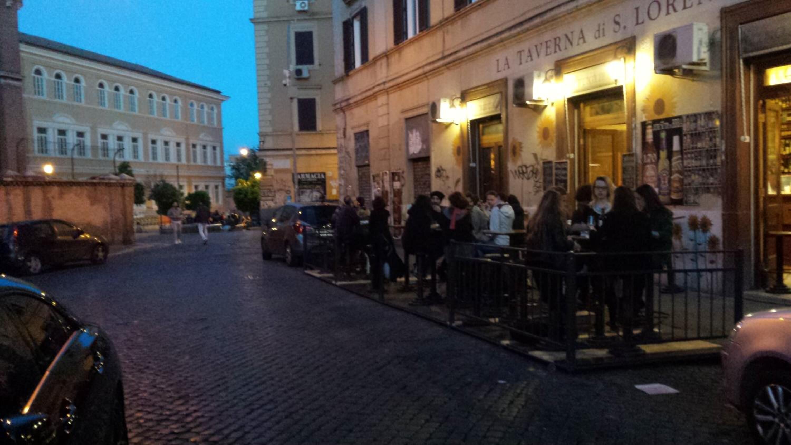 A street scene with a restaurant named "LA TAVERNA di S. LORENZO" and a building with classical architecture in the background.