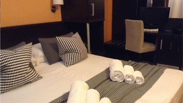 A hotel room with a neatly made bed, a grey and white checkered throw blanket, and a pair of rolled towels. - San Lorenzo Guest House (Rome)