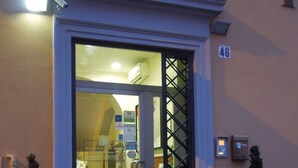 A hotel entrance with a glass door, a security camera, and a number '46' sign. There are two potted plants on either side of the door. - San Lorenzo Guest House (Rome)