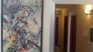 A hallway with a Kandinsky painting on the wall, a door, and a light fixture. - San Lorenzo Guest House (Rome)