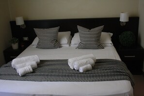A neatly made bed with a checkered pillowcase, a striped blanket, and rolled towels. - San Lorenzo Guest House (Rome)