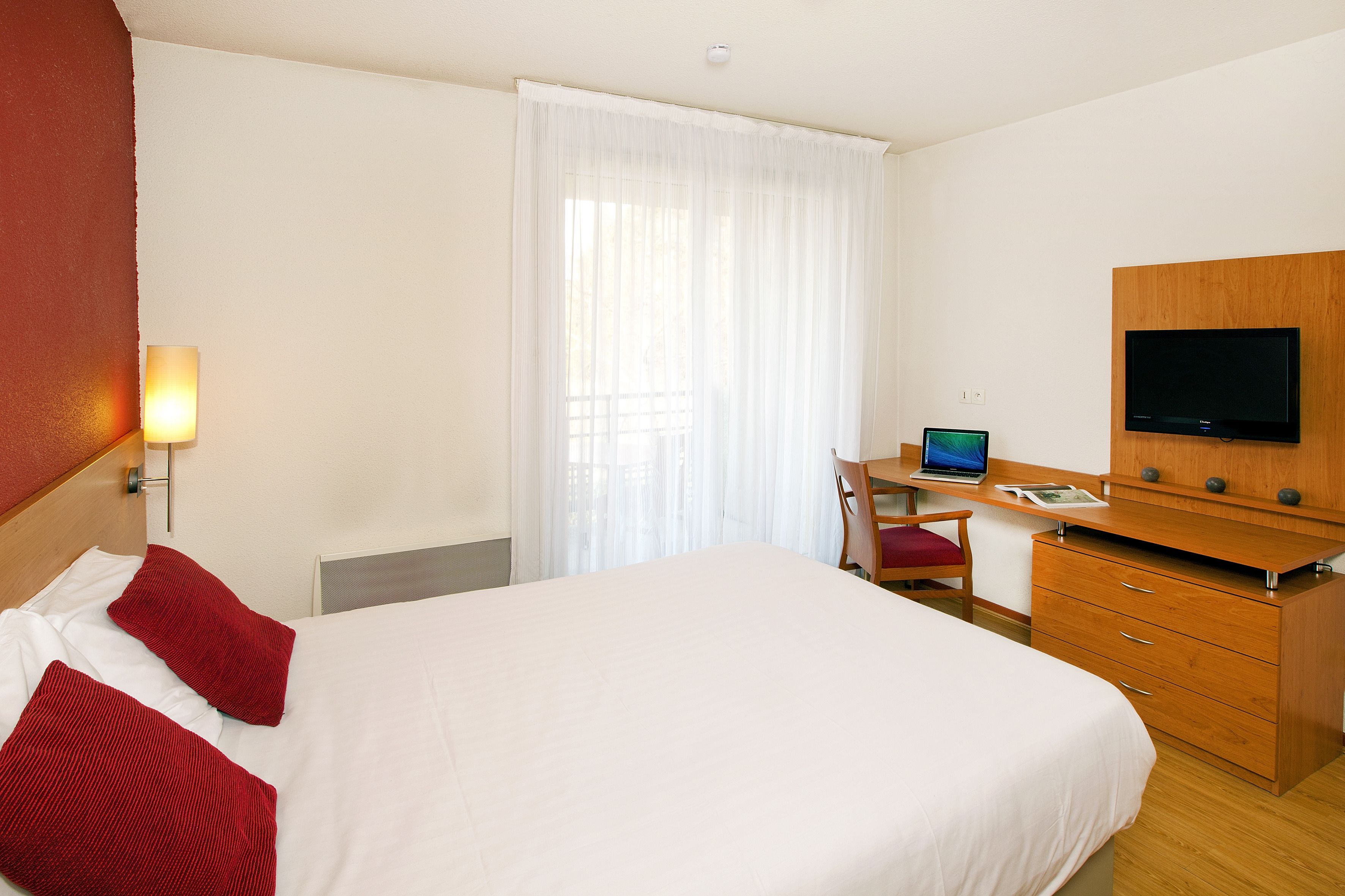 Une chambre d’hôtel comprenant un lit, un bureau avec un ordinateur portable, un téléviseur à écran plat et une commode en bois.