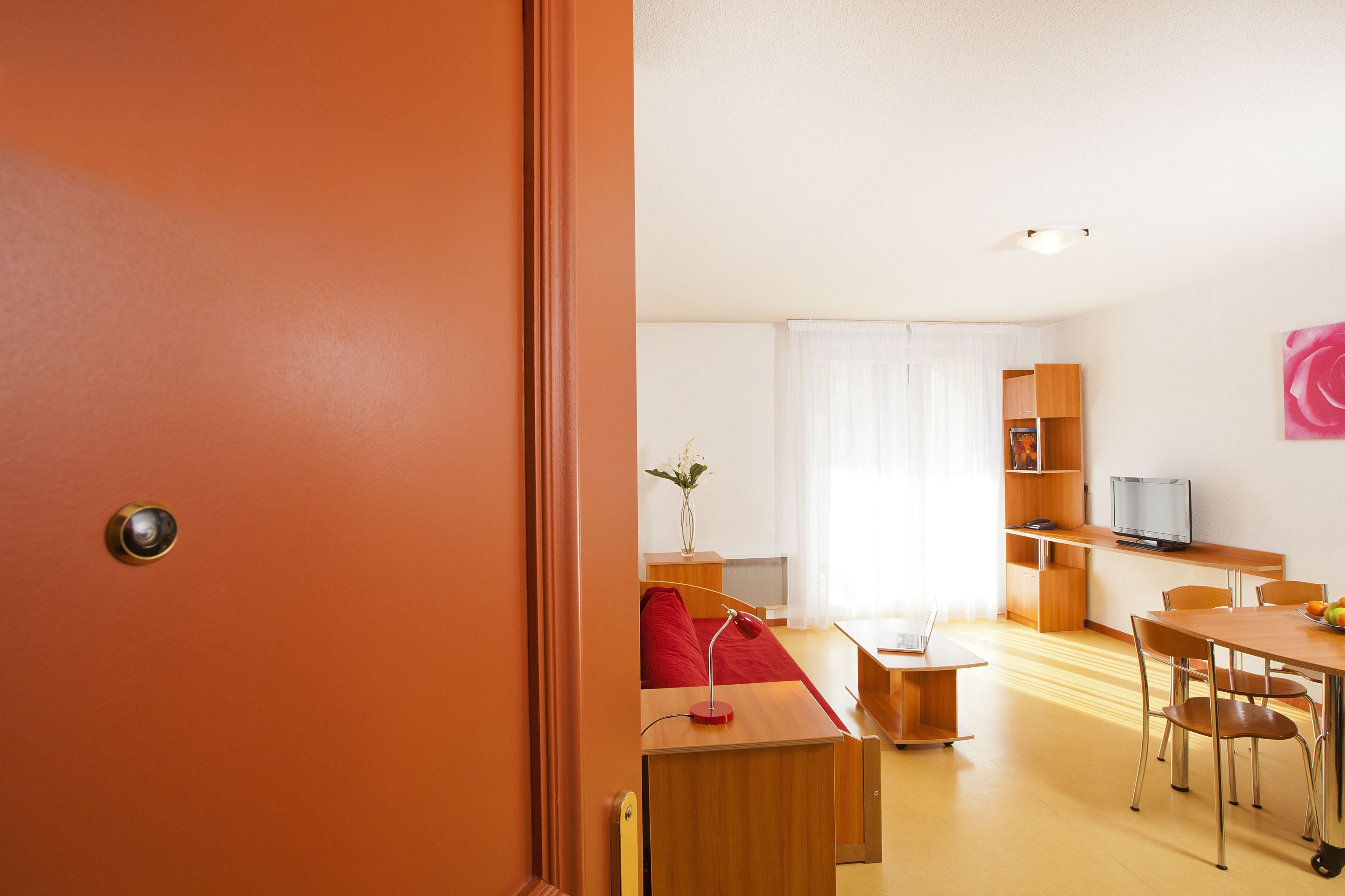 A modern living room with a red sofa, wooden furniture, a dining area, and a TV on a wooden shelf.