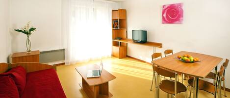 A compact living space with a bed, a dining table with chairs, a TV, and a bookshelf.