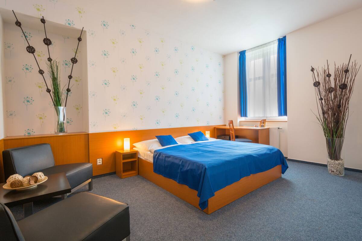 Una camera d'albergo con un letto, una scrivania, una sedia, un tavolino e un vaso con piante.