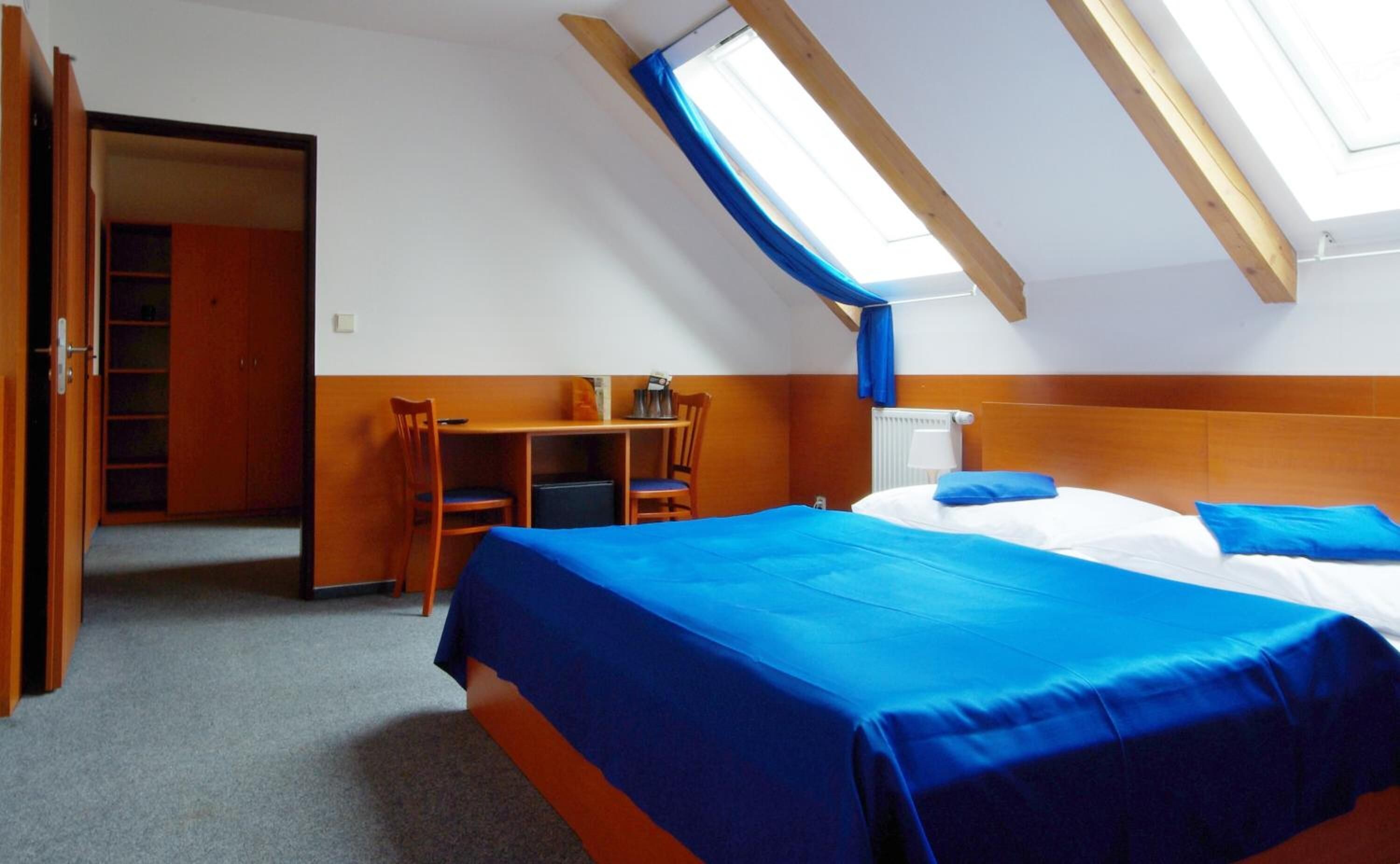 A room with a bed, a desk, and a chair. There is a window with blue curtains.