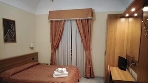Una habitación de hotel con cama, escritorio, televisor y armario.