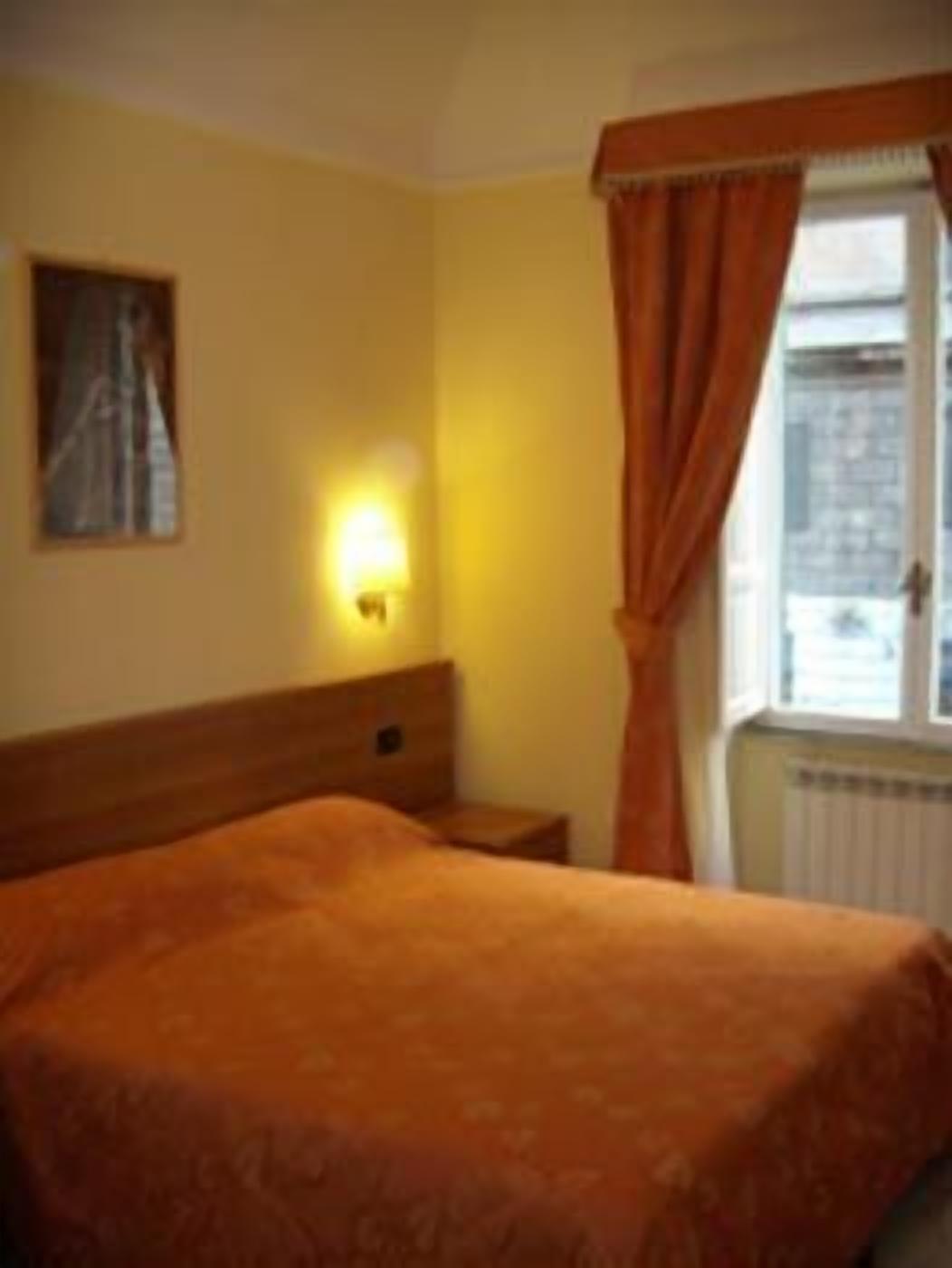 A hotel room with a single bed, a nightstand, a wall-mounted lamp, and a window with curtains.