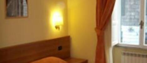 A hotel room with a single bed, a nightstand, a wall-mounted lamp, and a window with curtains.