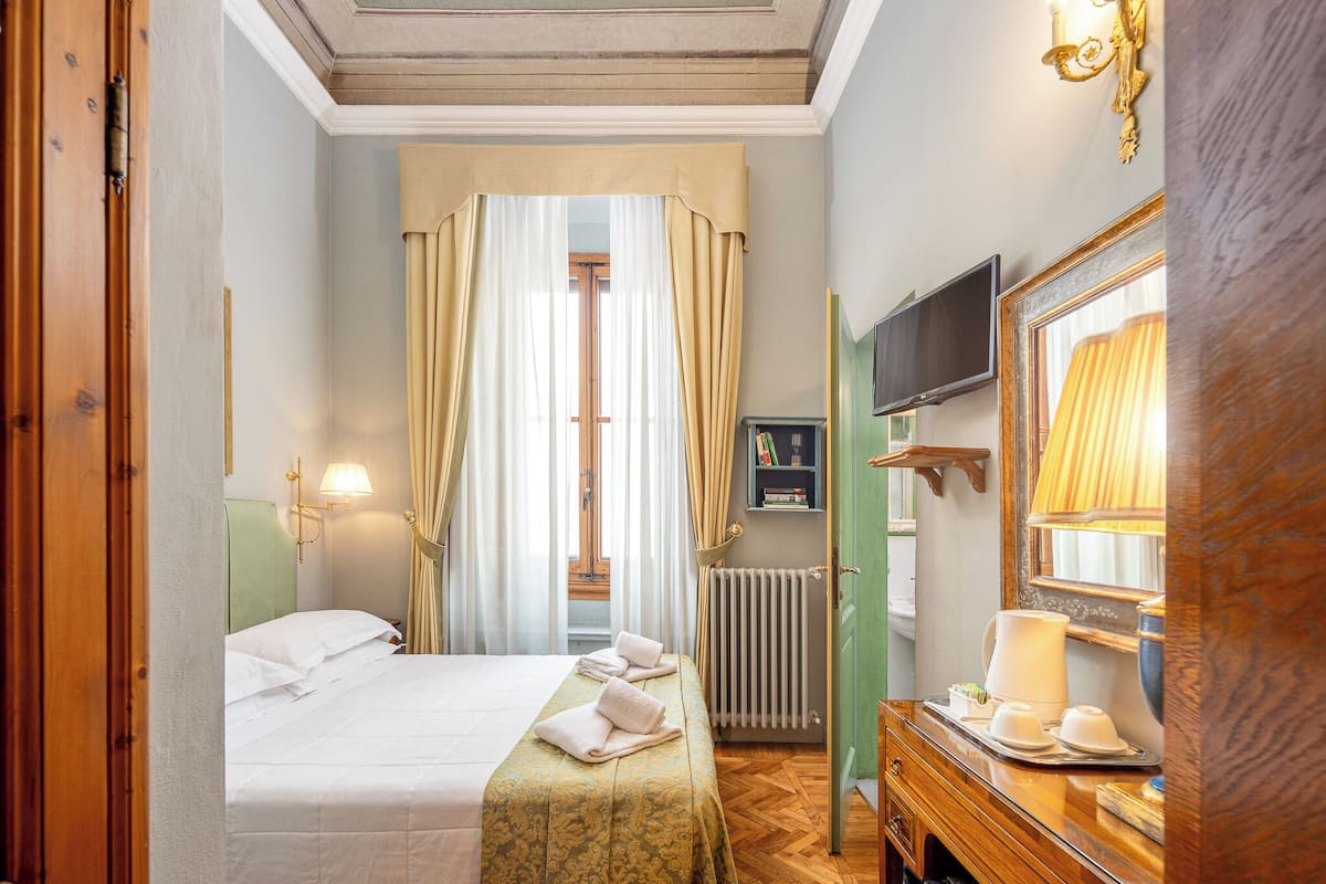 A hotel room with a bed, a desk with a mirror, a television, and a window with curtains.