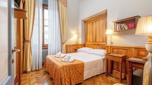 A hotel room with a bed, wooden headboard, bedside tables, a lamp, a bookshelf, and a window with curtains. - B&B Il Marzocco (Florence)