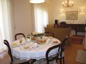 A dining area with a round table set for four, surrounded by chairs. There is a chandelier above the table, and a painting on the wall. - Marci's Home (Rome)