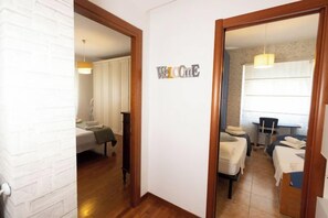 Ein Flur mit einem 'Welcome'-Schild, der zu einem Zimmer mit einem Bett und einem Schreibtisch führt.