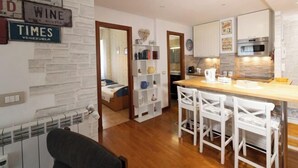 A modern kitchen with white cabinets, a wooden countertop, and a built-in oven. There is a dining area with white chairs and a small table. A bookshelf with various items is visible in the background. - Marci's Home (Rome)
