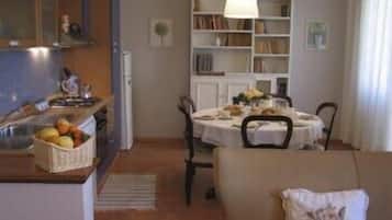 Un'accogliente sala da pranzo con un tavolo apparecchiato per due, una libreria e un angolo cottura con un cesto di frutta.