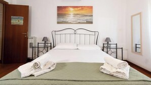 A hotel room with a bed, two bedside tables, a wall-mounted air conditioner, a painting of a sunset, a door, and a mirror. - Marci's Home (Rome)