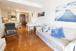 A modern living room with a wooden floor, a sofa with cushions, a dining area with a table and chairs, and a kitchen in the background. - Marci's Home (Rome)