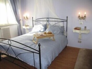 A neatly made bed with a tray, a bedside table, and a wall-mounted shelf with a lamp. - Marci's Home (Rome)