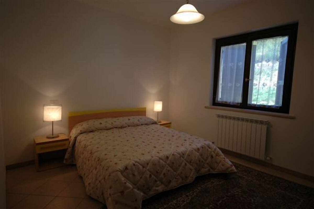 Ein Schlafzimmer mit einem Bett, zwei Nachttischlampen, einem Fenster mit Vorhängen und einer Heizung.
