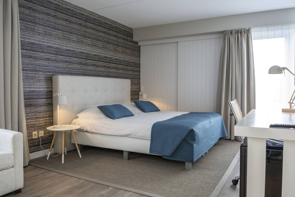 Ein modernes Hotelzimmer mit einem großen Bett, einem Schreibtisch und Blick auf die Stadt.