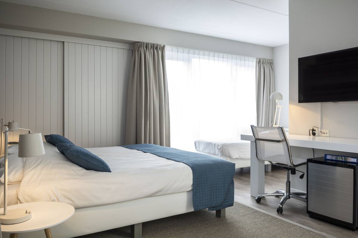 Ein Hotelzimmer mit Bett, Schreibtisch, Sessel, Fernseher und Lampe.