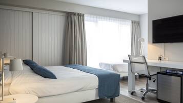 Ein Hotelzimmer mit Bett, Schreibtisch, Sessel, Fernseher und Lampe.