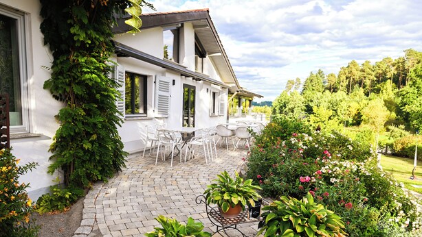 Un bâtiment blanc doté d’un patio avec jardin, d’un espace extérieur aménagé pour s’asseoir et de plantes en pot.