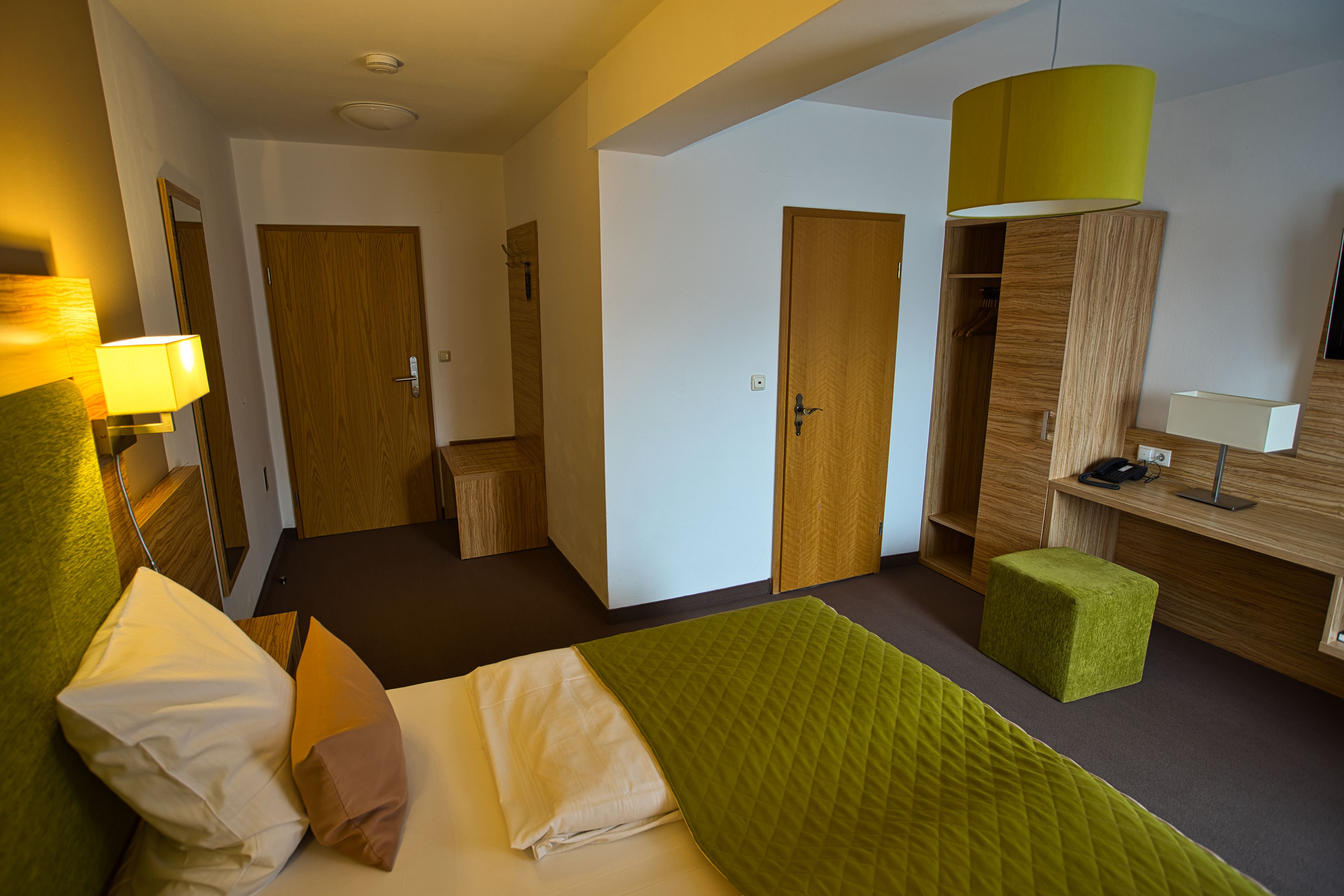Una habitación de hotel con cama, escritorio, silla, armario y espejo.