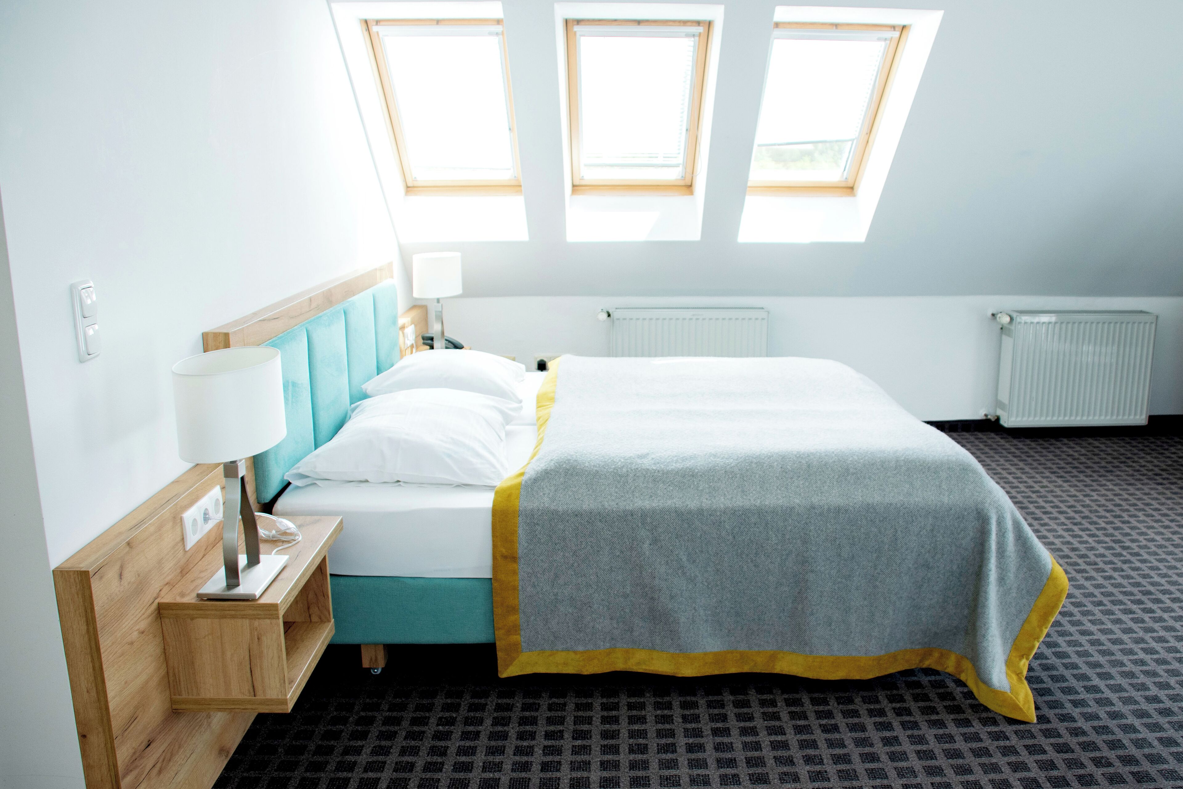 Hotellihuone, jossa on sänky, yöpöytä, lamppu ja ikkunasta avautuva näkymä taivaalle.