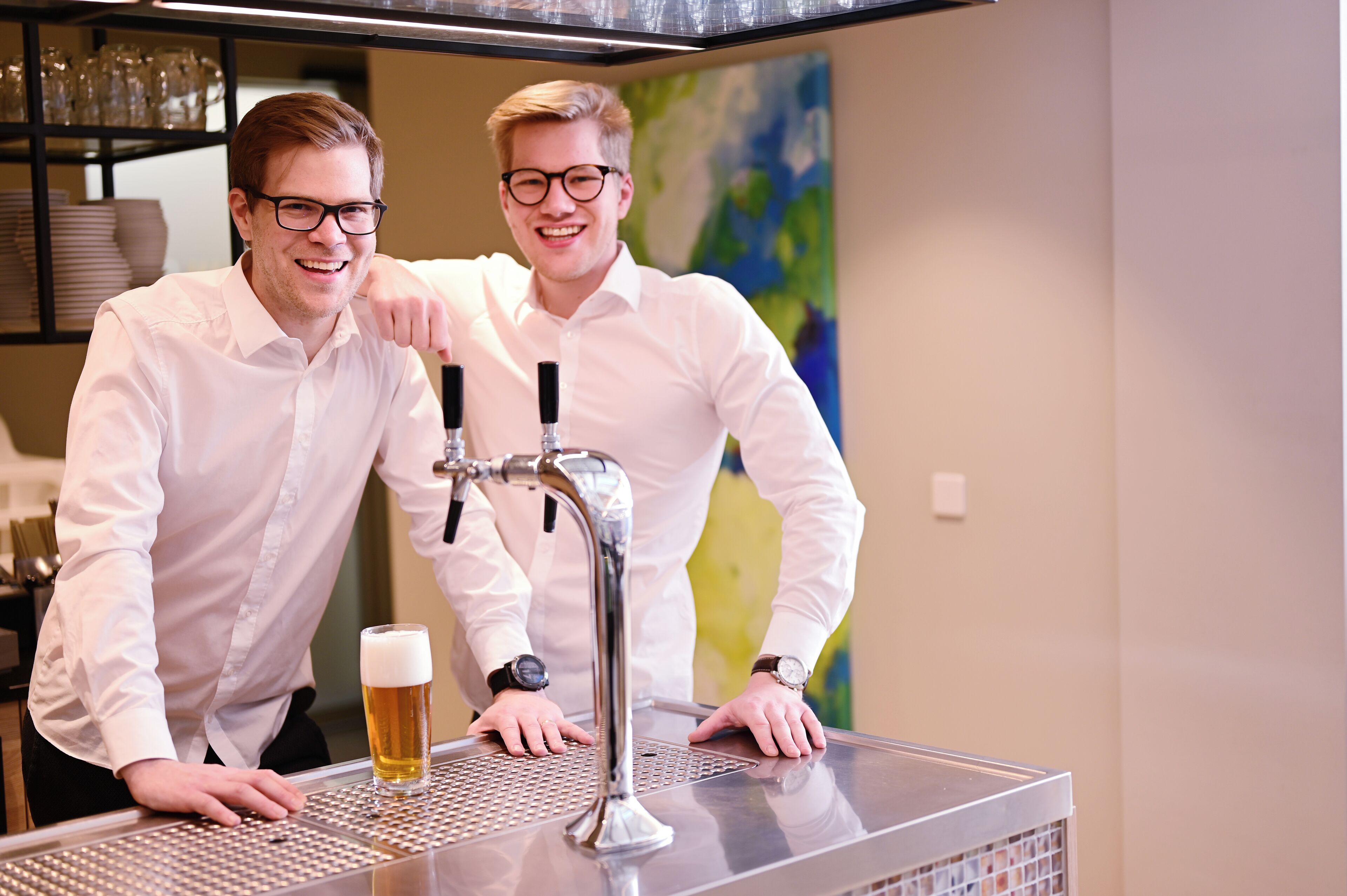Two individuals at a bar with a tap and a glass of beer.
