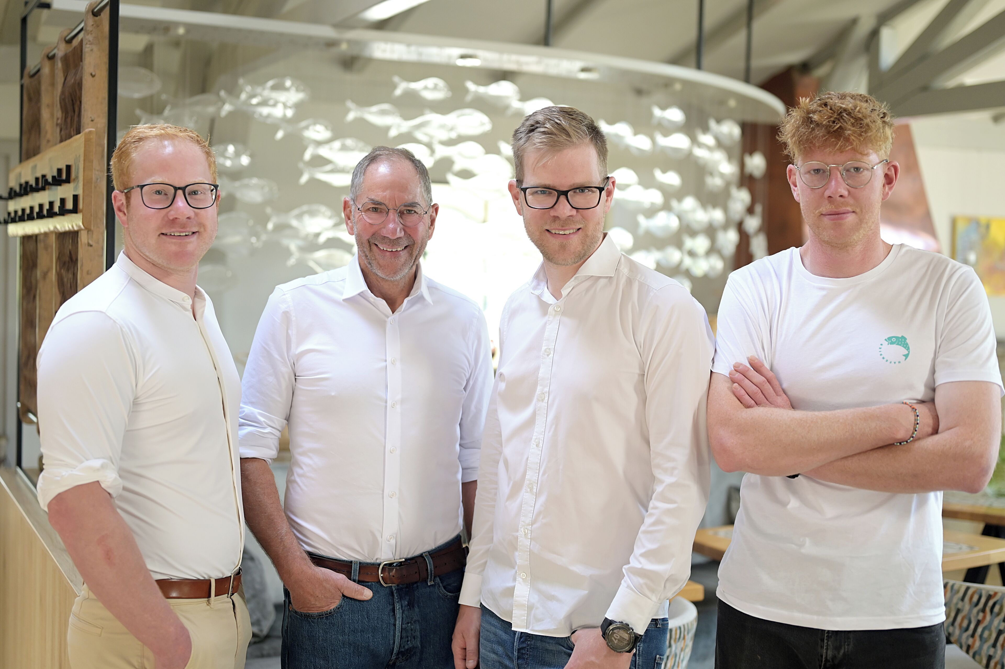 Four men standing in a room with a modern interior design, including a unique fish sculpture on the wall.