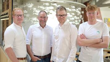 Four men standing in a room with a modern interior design, including a unique fish sculpture on the wall.