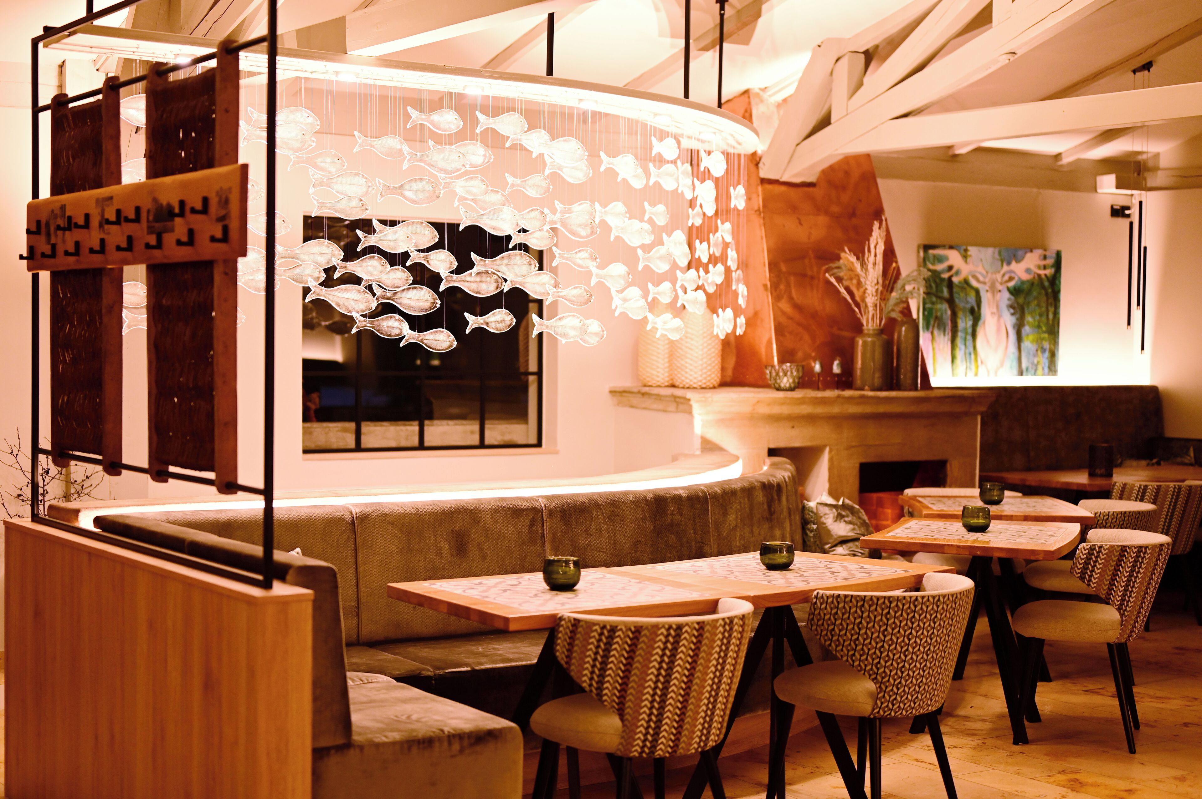 A restaurant with a curved counter, wooden tables, patterned chairs, and a decorative fish wall hanging.