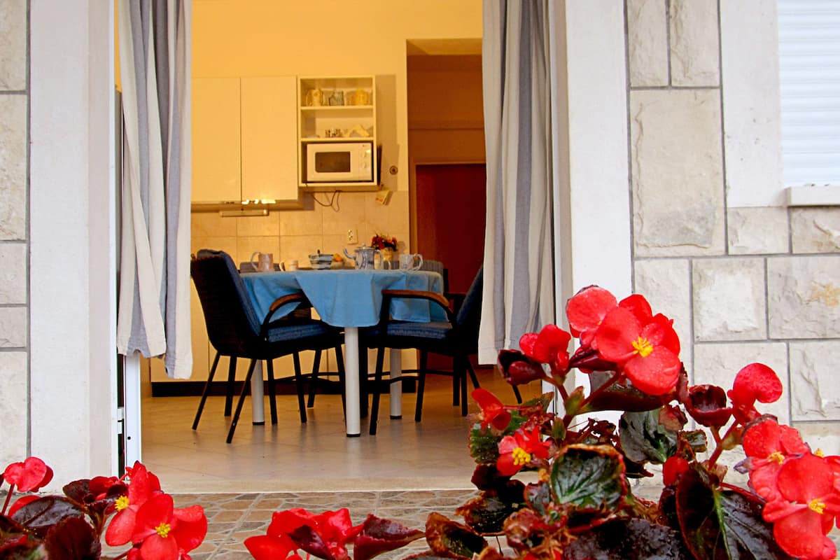 Un umbral abierto que da a un comedor con una mesa preparada para dos, sillas y una cocina visible al fondo.