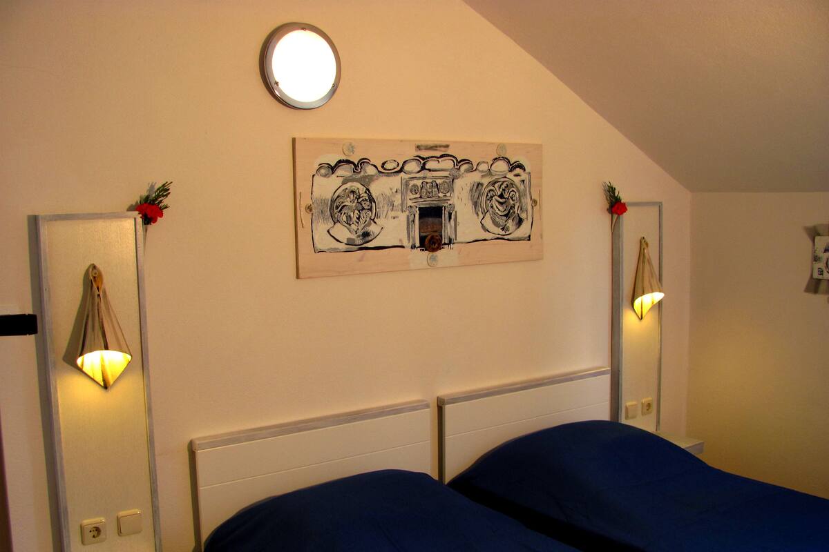 Un dormitorio con dos camas, una lámpara de techo y una obra de arte en la pared.