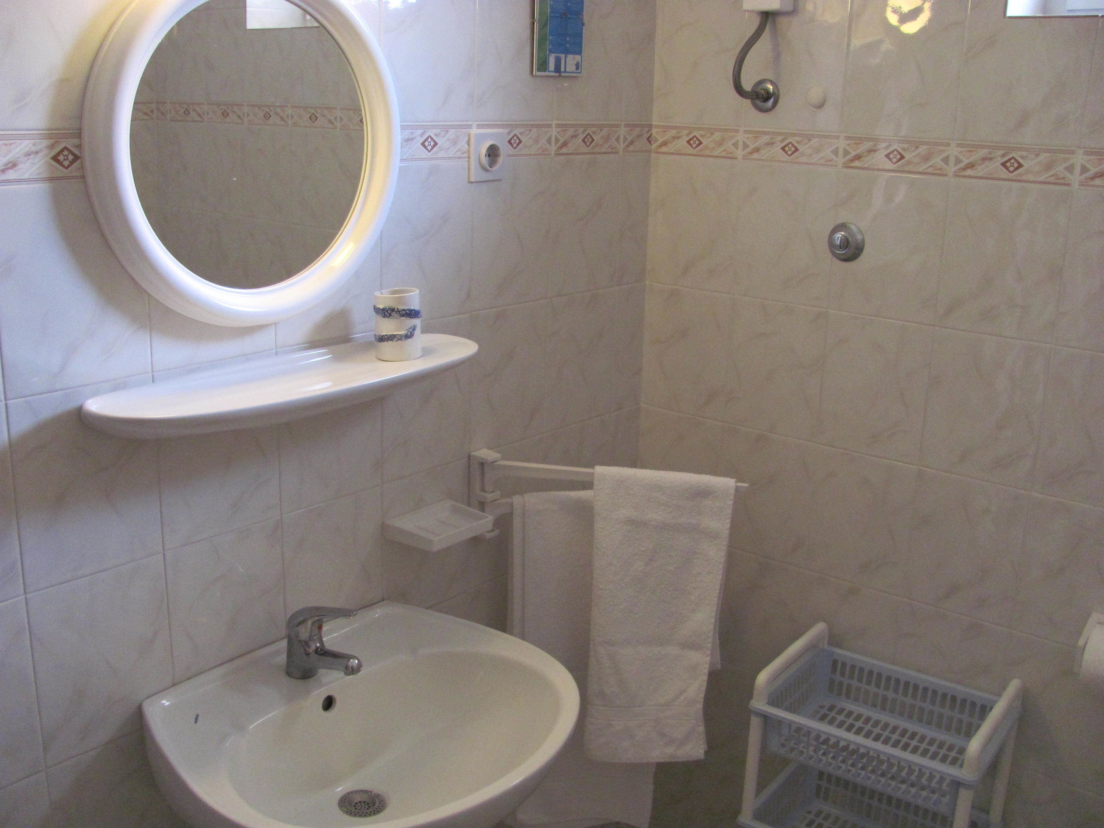 A bathroom with a sink, mirror, towel rack, and a small shelf with a cup.