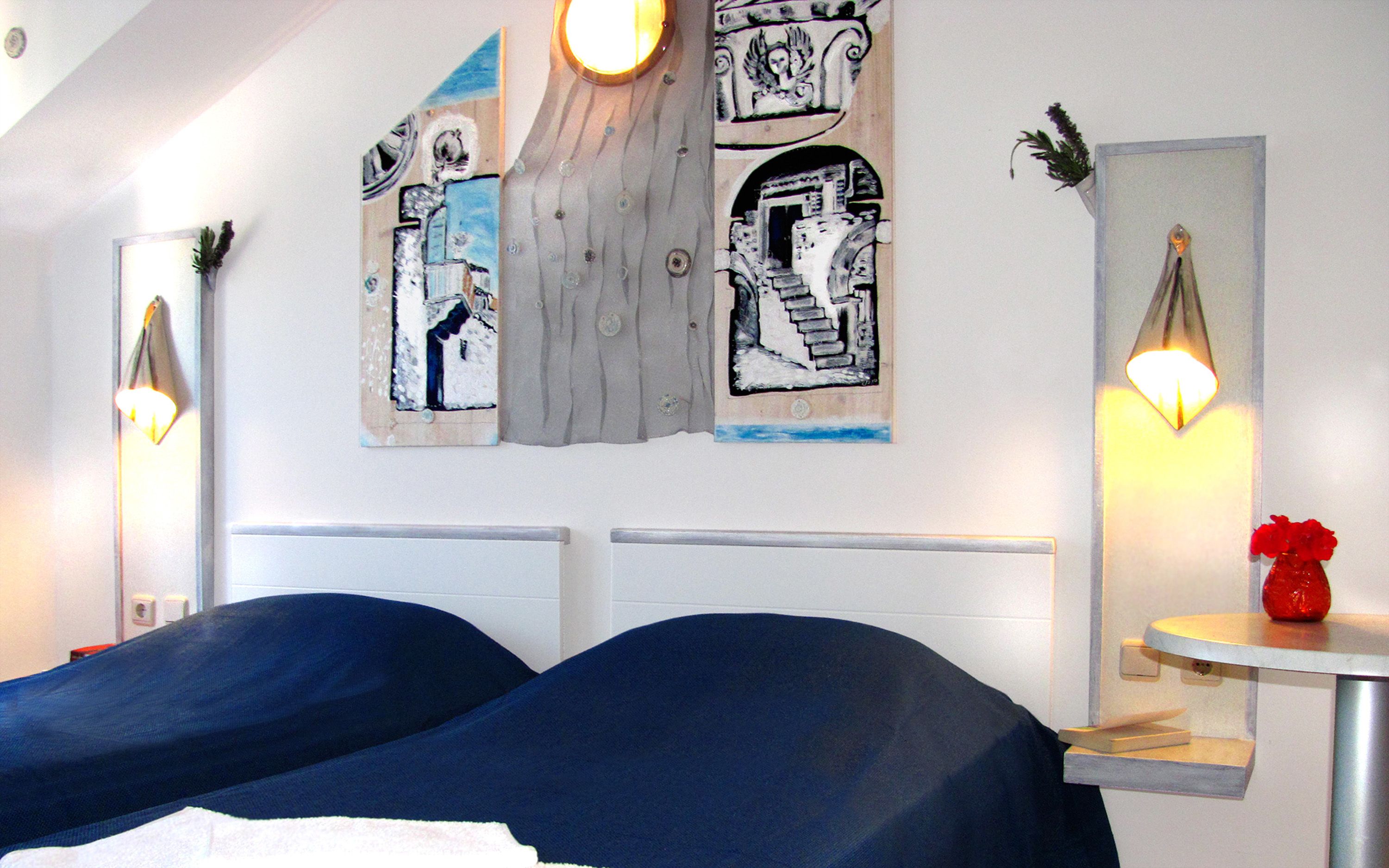 A hotel room with two beds, a small table with a red vase, and wall art.