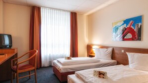 A hotel room with two beds, a desk with a chair, a television, and a painting on the wall. - Center Hotel Drive Inn (Hirschaid)