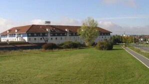 A large, white building with a red roof, surrounded by green grass and a few trees. - Center Hotel Drive Inn (Hirschaid)