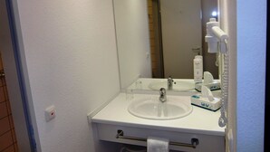A bathroom with a white sink, mirror, and towel rack. There is a handheld showerhead and a bottle of lotion on the counter. - Center Hotel Drive Inn (Hirschaid)